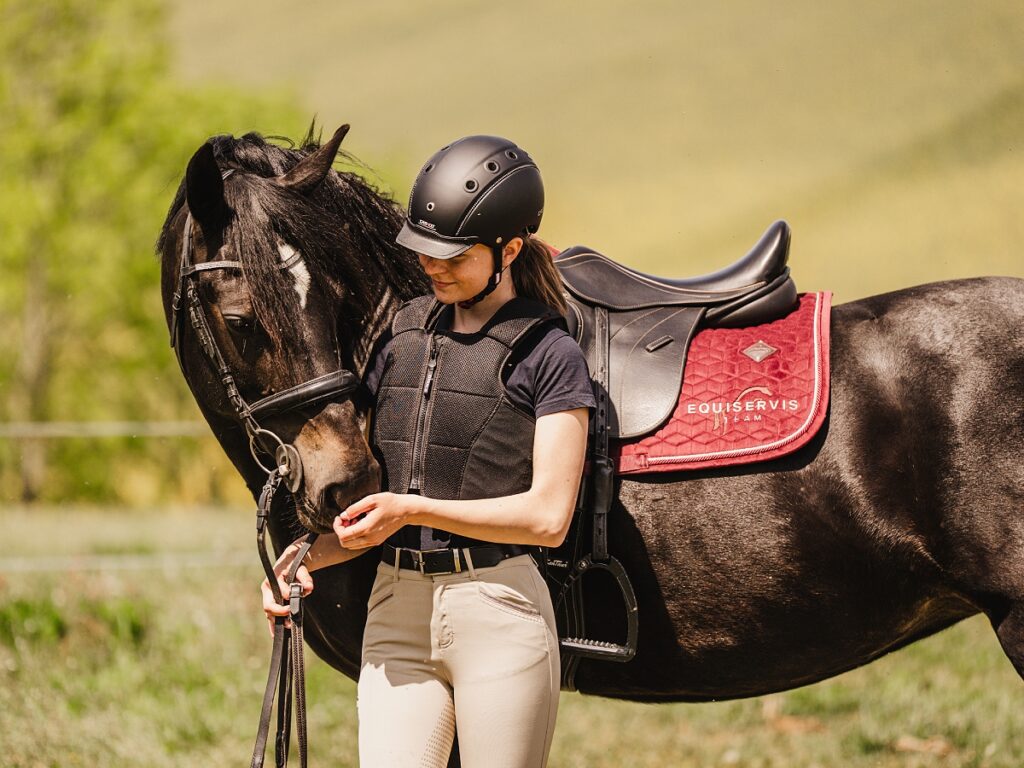 ZÁKLADNÍ VÝBAVA PRO ZAČÍNAJÍCÍ JEZDCE děvče s koněm v jezdecké helmě a vestě